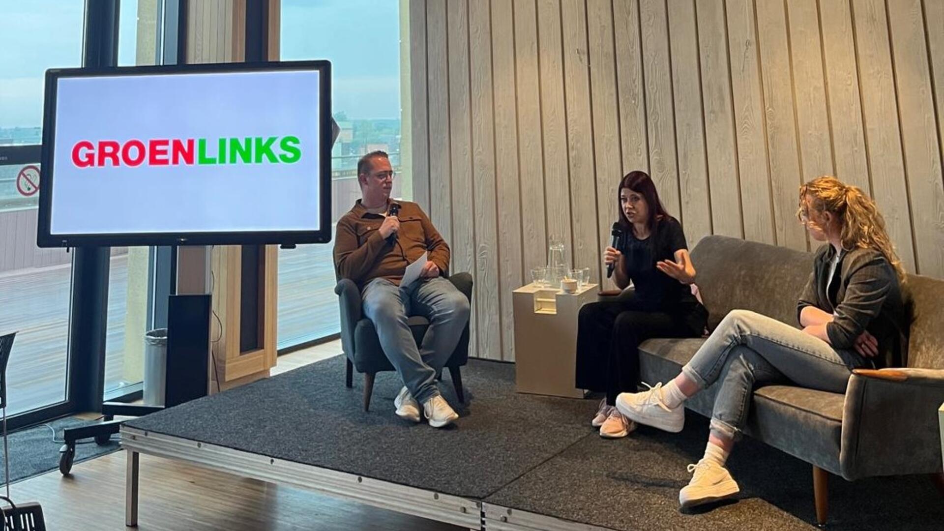 Rob, Lisa Westerveld, Marin Noomen op het podium met een scherm met het GroenLinks logo 